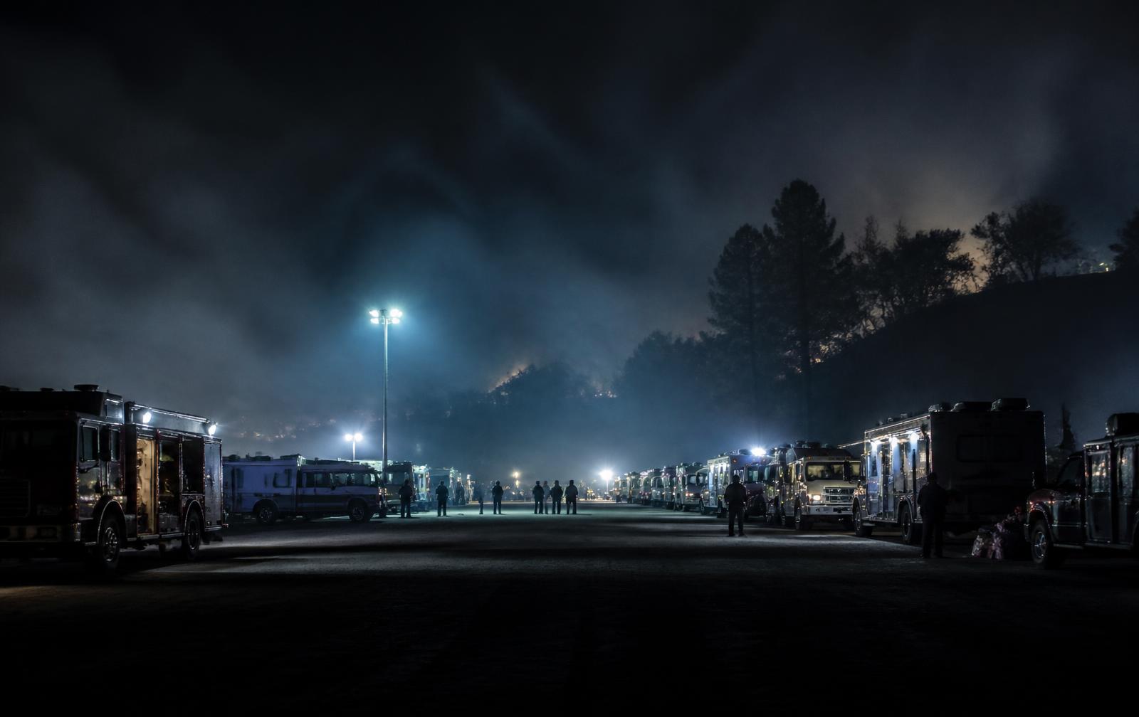 Emergency response vehicles staged at night under floodlights